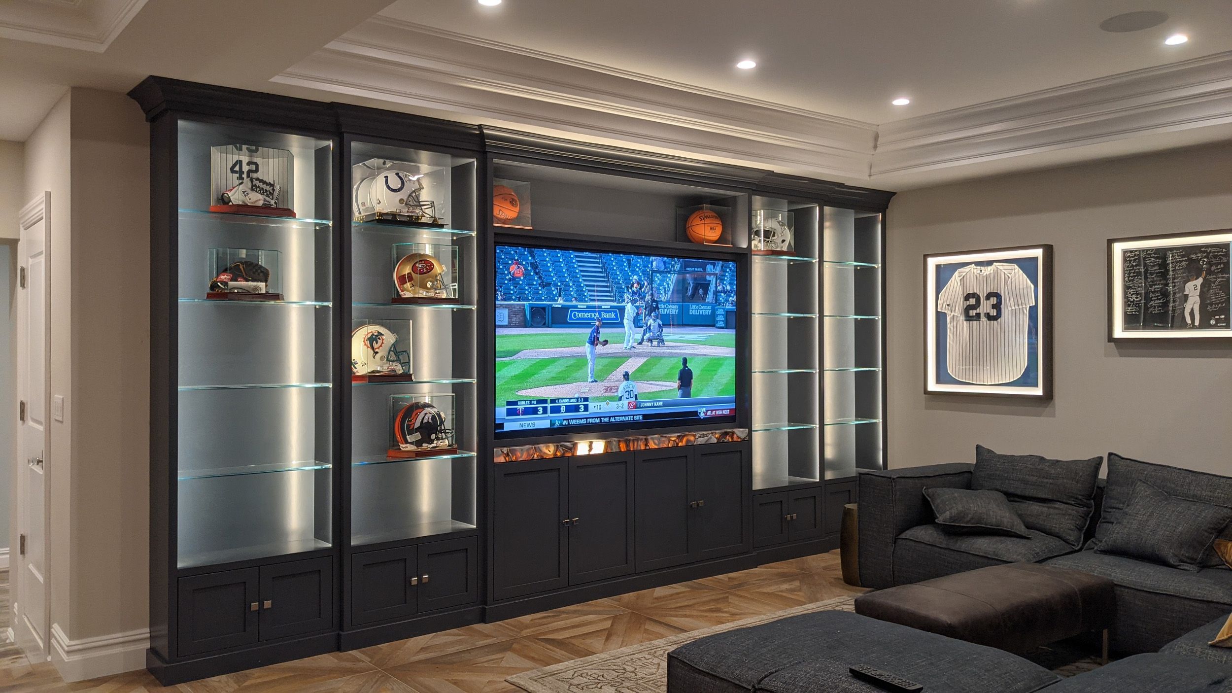 media room with tv showing a baseball game with collectible football helmets in cases next to the television